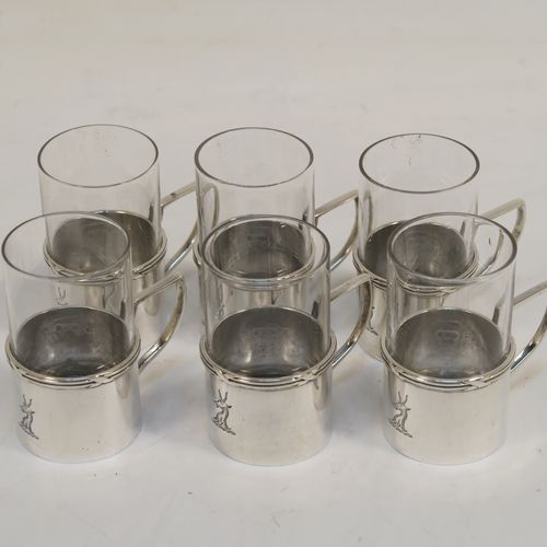 A handsome Antique Edwardian Sterling Silver and cut-glass set of six liqueor tots or measures, having plain round bodies with scroll side-handles and applied ribbon and reed top borders, and plain round glass inserts with star-cut bases. These elegant silver and cut-glass liquor tots were made by William Comyns of London in 1906. The dimensions of this fine hand-made antique silver liqueur tot set are height 5 cms (2 inches), diameter 3 cms (1.25 inches), and their total weight is approx. 84g (2.7 troy ounces). Please note that these are part-crested.