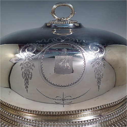 An Antique Georgian Old Sheffield plated meat cover dome and warming stand platter, having a plain oval body with Regency style gadroon and fluted border, a cast reeded loop handle, and all sitting on a well and tree dish for carving, having a hot water jacket, and with matching decoration, and sitting on four cushion feet. Made in the Regency period ca. 1815. The dimensions of this fine hand-made Old Sheffield plated meat cover dome and hot water stand are length (inc. handles) 53 cm (21 inches), width 42 cms (16.5 inches), and height 34 cms (13.5 inches). Please note that the meat dome is engraved and crested on one side.   