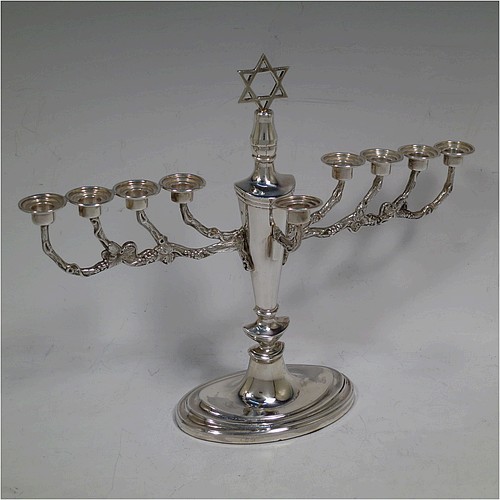 A pretty Sterling Silver Hanukkah Menorah, having a neoclassical style plain oval urn-shaped main body sitting on a pedestal foot, with cast grapevine style arms, and a removable Shamus candle holder. Made by D. J. Silver of London in 1970. The dimensions of this fine hand-made silver menorah are height 21 cms (8.25 inches), and spread across arms 26 cms (10.25 inches).   