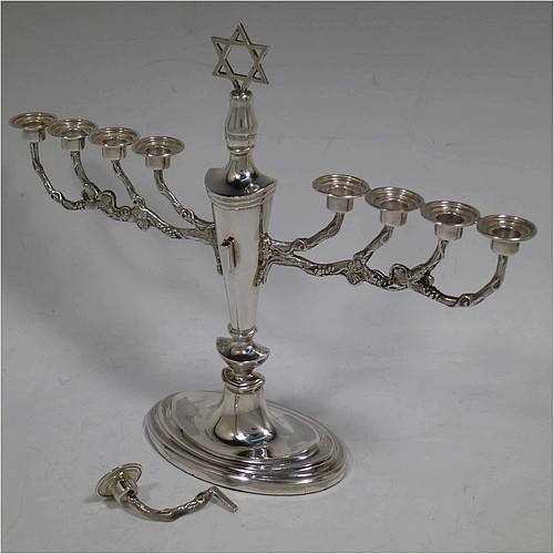 A pretty Sterling Silver Hanukkah Menorah, having a neoclassical style plain oval urn-shaped main body sitting on a pedestal foot, with cast grapevine style arms, and a removable Shamus candle holder. Made by D. J. Silver of London in 1970. The dimensions of this fine hand-made silver menorah are height 21 cms (8.25 inches), and spread across arms 26 cms (10.25 inches).   