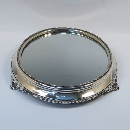 A very pretty Antique Victorian Sterling Silver mirror plateau, having a round body with an applied bead-edged top border surrounding the mirror, an applied gadroon-edged bottom border, all sitting on three cast foliate and shell feet, and an original oak base underneath. This elegant antique silver mirror plateau was made by Henry Woodward of Birmingham in 1876. The dimensions of this fine hand-made antique silver mirror plateau are diameter 29 cms (11.5 inches), and height 6 cms (2.3 inches).   