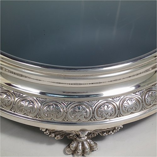 An Antique Edwardian Sterling Silver mirror plateau, having a round body with hand-chased floral decoration, a plain reeded border surrounding the mirror, all sitting on three cast foliate and lions-paw feet, and an original oak base underneath. Made by the Deakin Brothers of Sheffield in 1904. The dimensions of this fine hand-made antique silver mirror plateau are diameter 38 cms (15 inches), and height 9 cms (3.5 inches).    