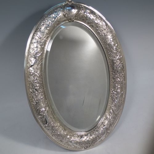 A very unusual and pretty Antique Victorian Sterling Silver table or vanity mirror (that also doubles as a mirror plateau), having hand-chased cherubs and floral work, surrounding an original bevelled oval mirror, and a blue velvet backing with eight stud feet and an easel stand. Made by Elkington and Co., of Birmingham in 1900. The dimensions across the frame of this fine hand-made antique silver vanity or table mirror are height 38 cms (15 inches), and width 27 cms (10.5 inches). Please note that the silver backing to the mirror has age-related marks, but nothing too serious.   