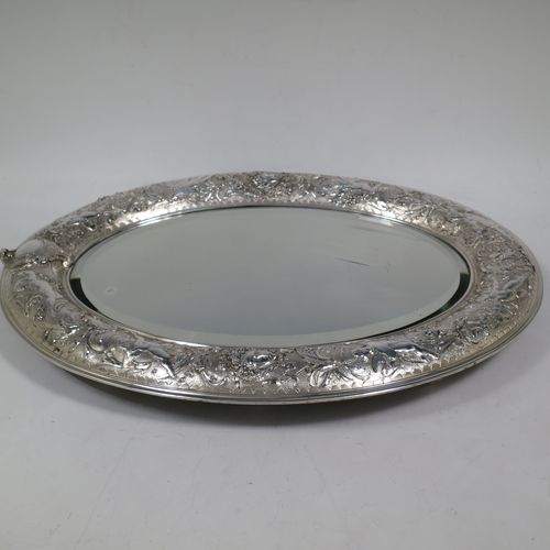 A very unusual and pretty Antique Victorian Sterling Silver table or vanity mirror (that also doubles as a mirror plateau), having hand-chased cherubs and floral work, surrounding an original bevelled oval mirror, and a blue velvet backing with eight stud feet and an easel stand. Made by Elkington and Co., of Birmingham in 1900. The dimensions across the frame of this fine hand-made antique silver vanity or table mirror are height 38 cms (15 inches), and width 27 cms (10.5 inches). Please note that the silver backing to the mirror has age-related marks, but nothing too serious.   