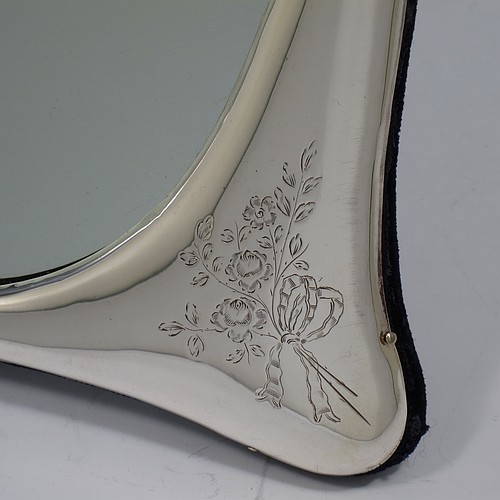 A very pretty Antique Edwardian Sterling Silver table or vanity mirror having hand-engraved floral work with ribbon and bow decoration, surrounding an oval mirror, and a blue velvet backing with easel stand. Made by the Alexander Clark Manufacturing Company of Birmingham in 1910. The dimensions across the frame of this fine hand-made antique silver vanity or table mirror are height 33 cms (13 inches), and width 21 cms (8.25 inches).   