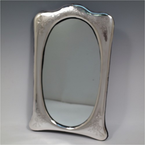 A very pretty Antique Edwardian Sterling Silver table or vanity mirror having hand-engraved floral work with ribbon and bow decoration, surrounding an oval mirror, and a blue velvet backing with easel stand. Made by the Alexander Clark Manufacturing Company of Birmingham in 1910. The dimensions across the frame of this fine hand-made antique silver vanity or table mirror are height 33 cms (13 inches), and width 21 cms (8.25 inches).   