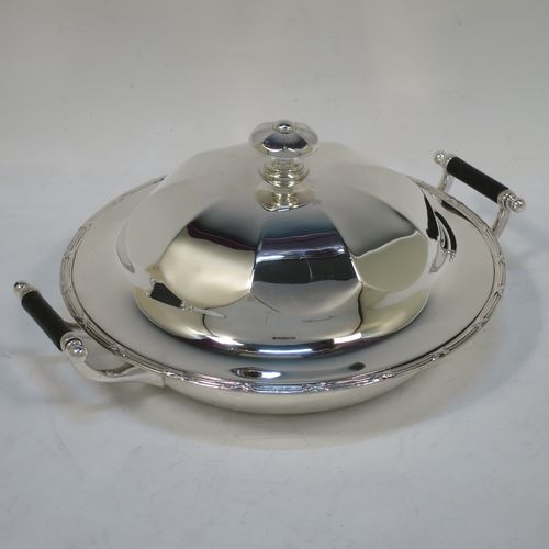 A handsome Antique Sterling Silver muffin dish, having a round body with an applied ribbon and reed border, with two side handles having black ebonised inserts, a domed and panelled lift-off lid with cast finial, and all sitting on a flat base. Made by James Dixon and Sons of Sheffield in 1911. The dimensions of this fine hand-made antique silver muffin dish are diameter 18 cms (7 inches), height 9 cms (3.5 inches), and it weighs approx. 330g (10.6 troy ounces).  