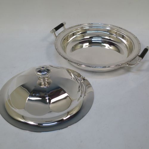 A handsome Antique Sterling Silver muffin dish, having a round body with an applied ribbon and reed border, with two side handles having black ebonised inserts, a domed and panelled lift-off lid with cast finial, and all sitting on a flat base. Made by James Dixon and Sons of Sheffield in 1911. The dimensions of this fine hand-made antique silver muffin dish are diameter 18 cms (7 inches), height 9 cms (3.5 inches), and it weighs approx. 330g (10.6 troy ounces).  