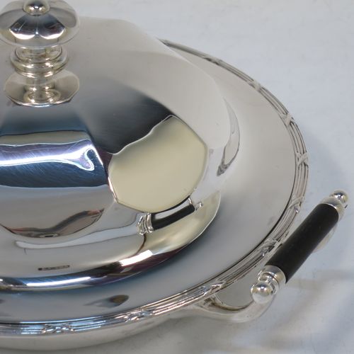 A handsome Antique Sterling Silver muffin dish, having a round body with an applied ribbon and reed border, with two side handles having black ebonised inserts, a domed and panelled lift-off lid with cast finial, and all sitting on a flat base. Made by James Dixon and Sons of Sheffield in 1911. The dimensions of this fine hand-made antique silver muffin dish are diameter 18 cms (7 inches), height 9 cms (3.5 inches), and it weighs approx. 330g (10.6 troy ounces).  