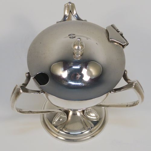 A very stylish Antique Edwardian Art Nouveau mustard pot, having a plain round bellied body, with a hinged lid and a cast urn finial, and three scroll side-handles attached to a round pedestal foot, and with an internal blue glass liner. This silver Art Nouveau mustard pot was made by Edward Souter Barnsley of Birmingham in 1905. The dimensions of this fine hand-made antique silver mustard pot are height 8 cms (3 inches), diameter 5.5 cms (2.25 inches), and it weighs approx. 83g (2.7 troy ounces).   