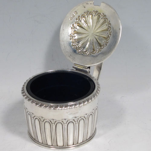 Antique Georgian Regency sterling silver mustard pot, having a round body with hand-chased fluted straight sides, a gadroon-edged border, a hinged lid with shell thumb-piece, a blue glass liner and scroll handle, all sitting on a flat base. Made by Rebecca Emes and Edward Barnard of London in 1817. The dimensions of this fine hand-made silver mustard pot are height 6.5 cms (2.5 inches), diameter 7 cms (2.75 inches), and it weighs approx. 146g (4.7 troy ounces).