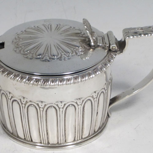 Antique Georgian Regency sterling silver mustard pot, having a round body with hand-chased fluted straight sides, a gadroon-edged border, a hinged lid with shell thumb-piece, a blue glass liner and scroll handle, all sitting on a flat base. Made by Rebecca Emes and Edward Barnard of London in 1817. The dimensions of this fine hand-made silver mustard pot are height 6.5 cms (2.5 inches), diameter 7 cms (2.75 inches), and it weighs approx. 146g (4.7 troy ounces).