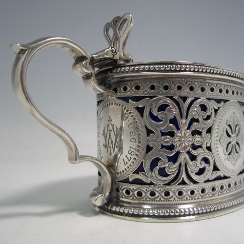 Antique Victorian sterling silver mustard pot, having an oval straight-sided body with beautiful hand-pierced and engraved floral decoration, with applied bead borders, a hinged flat lid with hand-pierced thumb-piece, a scroll handle and a blue glass liner. Made by the Barnard Brothers of London in 1875. The dimensions of this fine hand-made silver mustard pot are height 7 cms (2.75 inches), length 11 cms (4.25 inches), and it weighs approx. 140g (4.5 troy ounces). Please note that this item is crested and monogrammed.   