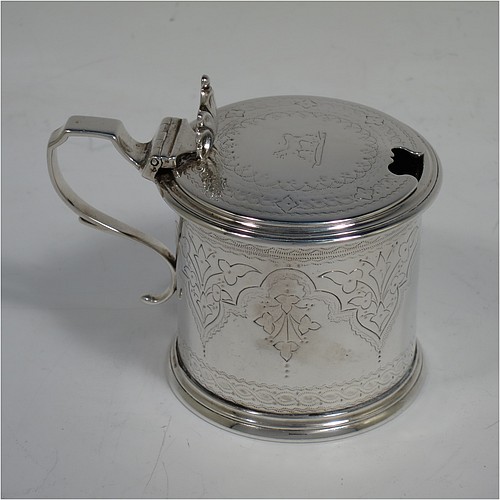 A very pretty Antique Victorian Sterling Silver drum mustard, having a cylindrical body with hand-engraved floral and scroll decoration, with applied reeded borders, a hinged flat lid with a cast floral thumb-piece, a scroll handle and a blue glass liner. Made by Edward Barnard of London in 1875. The dimensions of this fine hand-made antique silver mustard pot are height 8 cms (3 inches), diameter 6.5 cms (2.5 inches), and it weighs approx. 125g (4 troy ounces). Please note that this item is crested on the lid.   