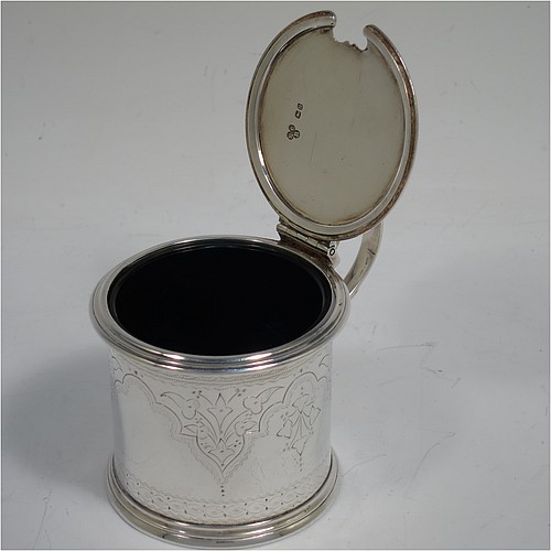 A very pretty Antique Victorian Sterling Silver drum mustard, having a cylindrical body with hand-engraved floral and scroll decoration, with applied reeded borders, a hinged flat lid with a cast floral thumb-piece, a scroll handle and a blue glass liner. Made by Edward Barnard of London in 1875. The dimensions of this fine hand-made antique silver mustard pot are height 8 cms (3 inches), diameter 6.5 cms (2.5 inches), and it weighs approx. 125g (4 troy ounces). Please note that this item is crested on the lid.   