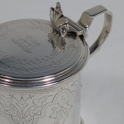 A very pretty Antique Victorian Sterling Silver drum mustard, having a cylindrical body with hand-engraved floral and scroll decoration, with applied reeded borders, a hinged flat lid with a cast floral thumb-piece, a scroll handle and a blue glass liner. Made by Edward Barnard of London in 1875. The dimensions of this fine hand-made antique silver mustard pot are height 8 cms (3 inches), diameter 6.5 cms (2.5 inches), and it weighs approx. 125g (4 troy ounces). Please note that this item is crested on the lid.   