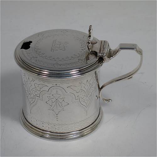 A very pretty Antique Victorian Sterling Silver drum mustard, having a cylindrical body with hand-engraved floral and scroll decoration, with applied reeded borders, a hinged flat lid with a cast floral thumb-piece, a scroll handle and a blue glass liner. Made by Edward Barnard of London in 1875. The dimensions of this fine hand-made antique silver mustard pot are height 8 cms (3 inches), diameter 6.5 cms (2.5 inches), and it weighs approx. 125g (4 troy ounces). Please note that this item is crested on the lid.   