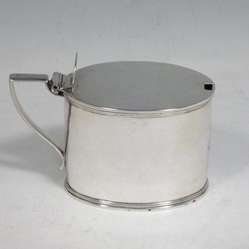 Antique Georgian sterling silver drum mustard pot, having a plain oval body with applied reeded borders, a flat hinged lid with thumb-piece, a scroll handle, and a blue-glass liner. Made by John Emes of London in 1804. The dimensions of this fine hand-made silver mustard pot are length 10 cms (4 inches), height 7.5 cms (3 inches), width 5 cms (2 inches), and it weighs approx. 137g (4.4 troy ounces). Please note that this item is crested.