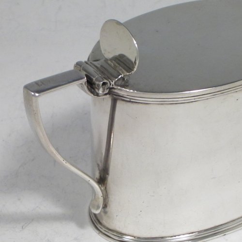 Antique Georgian sterling silver drum mustard pot, having a plain oval body with applied reeded borders, a flat hinged lid with thumb-piece, a scroll handle, and a blue-glass liner. Made by John Emes of London in 1804. The dimensions of this fine hand-made silver mustard pot are length 10 cms (4 inches), height 7.5 cms (3 inches), width 5 cms (2 inches), and it weighs approx. 137g (4.4 troy ounces). Please note that this item is crested.