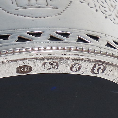 
An Antique Georgian Neoclassical Sterling Silver mustard pot, having an oval body with straight sides, with hand-pierced and engraved neoclassical style floral decoration, a hinged and domed lid with urn shaped finial and pierced thumb-pierce, a scroll handle, a blue glass liner, and all sitting on a flat base. Made by Robert Hennell I  of London in 1773. The dimensions of this fine hand-made antique silver mustard pot are height 8 cms (3.25 inches), length 10 cms (4 inches), width 5.5 cms (2.25 inches), and it weighs approx. 93g (3 troy ounces).    