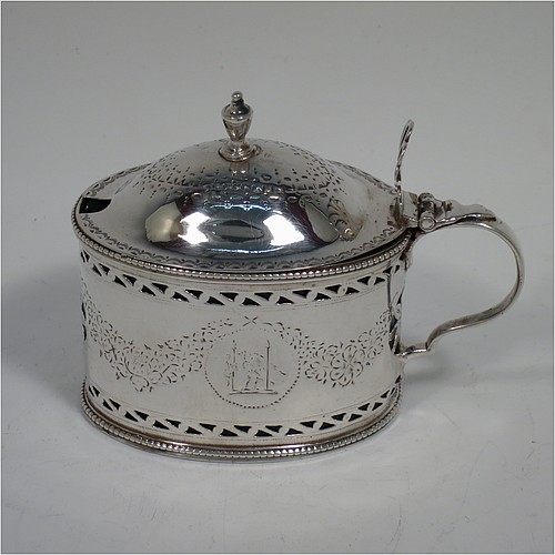 
An Antique Georgian Neoclassical Sterling Silver mustard pot, having an oval body with straight sides, with hand-pierced and engraved neoclassical style floral decoration, a hinged and domed lid with urn shaped finial and pierced thumb-pierce, a scroll handle, a blue glass liner, and all sitting on a flat base. Made by Robert Hennell I  of London in 1773. The dimensions of this fine hand-made antique silver mustard pot are height 8 cms (3.25 inches), length 10 cms (4 inches), width 5.5 cms (2.25 inches), and it weighs approx. 93g (3 troy ounces).    