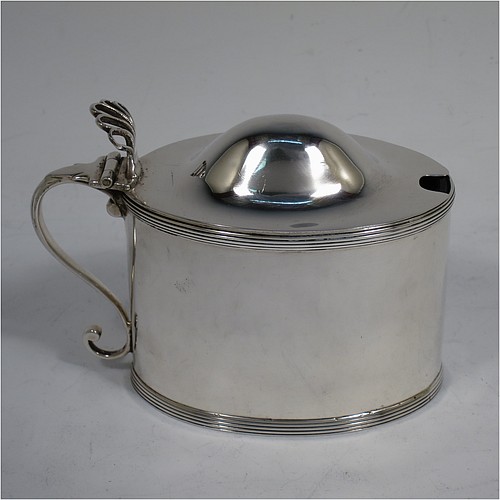 A very handsome Antique Georgian Sterling Silver mustard pot, having a plain oval straight-sided body, with applied reeded borders, a hinged domed lid with hand-pierced thumb-piece, a scroll side-handle, a blue-glass liner, and sitting on a flat base. Made by Peter and Anne Bateman of London in 1792. The dimensions of this fine hand-made antique silver mustard pot are length 10 cms (4 inches), height 7.5 cms (3 inches), and it weighs approx. 106g (3.4 troy ounces).   