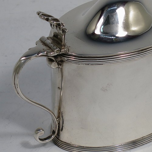 A very handsome Antique Georgian Sterling Silver mustard pot, having a plain oval straight-sided body, with applied reeded borders, a hinged domed lid with hand-pierced thumb-piece, a scroll side-handle, a blue-glass liner, and sitting on a flat base. Made by Peter and Anne Bateman of London in 1792. The dimensions of this fine hand-made antique silver mustard pot are length 10 cms (4 inches), height 7.5 cms (3 inches), and it weighs approx. 106g (3.4 troy ounces).   