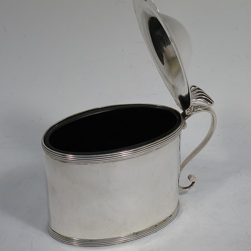 A very handsome Antique Georgian Sterling Silver mustard pot, having a plain oval straight-sided body, with applied reeded borders, a hinged domed lid with hand-pierced thumb-piece, a scroll side-handle, a blue-glass liner, and sitting on a flat base. Made by Peter and Anne Bateman of London in 1792. The dimensions of this fine hand-made antique silver mustard pot are length 10 cms (4 inches), height 7.5 cms (3 inches), and it weighs approx. 106g (3.4 troy ounces).   