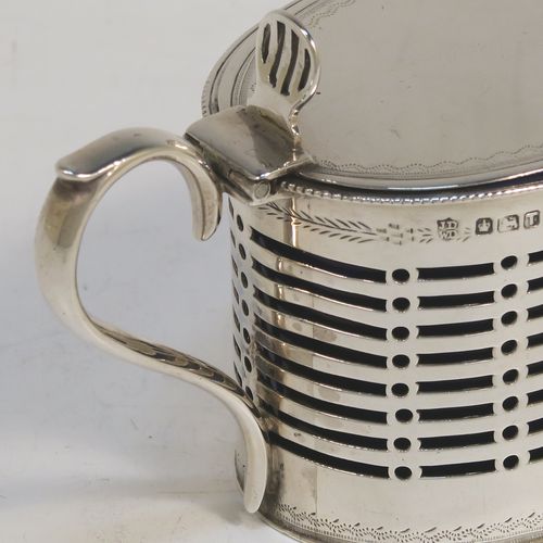 A very handsome Antique Victorian Sterling Silver mustard pot, having an oval straight-sided body with hand-pierced geometrical decoration, with hand-engraved floral borders, a hinged flat lid with hand-pierced thumb-piece, a scroll handle, and a blue glass liner. This beautiful silver mustard pot was made by James and Walter Deakin of Sheffield in 1886. The dimensions of this fine hand-made antique silver mustard pot are height 7 cms (2.75 inches), length 10 cms (4 inches), and it weighs approx. 77g (2.5 troy ounces).   