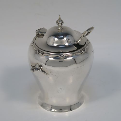 An unusual and rare Antique Edwardian Art Nouveau mustard pot, having a plain round bellied body with two cast scroll side-handles, an applied scroll style top border, a hinged lid with a cast urn finial, an internal blue glass liner, and all sitting on a flat base. This beautiful silver mustard pot comes with a garden shovel style silver spoon. This elegant silver Art Nouveau mustard pot was made by Jackson and Fullerton of London in 1909. The dimensions of this fine hand-made antique silver mustard pot are height 10 cms (4 inches), diameter 7 cms (2.75 inches), and it weighs approx. 114g (3.7 troy ounces).  