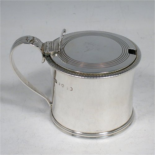 An Antique Georgian Sterling Silver drum mustard pot, having a plain round body with an applied gadroon border, a slightly domed hinged lid with a hand-engraved reeded band and a pierced thumb-piece, a scroll reeded handle with an applied anthemion leaf, and a blue-glass liner. Made by Richard Palmer I of London in 1821. The dimensions of this fine hand-made antique silver mustard pot are length 10 cms (4 inches), height 7.5 cms (3 inches), and it weighs approx. 155g (5 troy ounces). Please note that this item is crested on the lid.