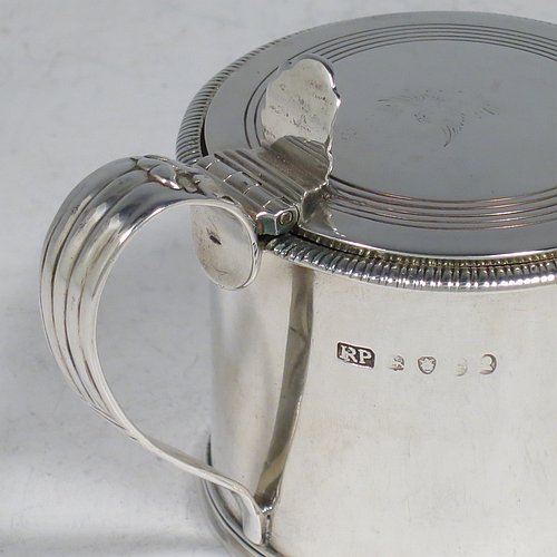 An Antique Georgian Sterling Silver drum mustard pot, having a plain round body with an applied gadroon border, a slightly domed hinged lid with a hand-engraved reeded band and a pierced thumb-piece, a scroll reeded handle with an applied anthemion leaf, and a blue-glass liner. Made by Richard Palmer I of London in 1821. The dimensions of this fine hand-made antique silver mustard pot are length 10 cms (4 inches), height 7.5 cms (3 inches), and it weighs approx. 155g (5 troy ounces). Please note that this item is crested on the lid.