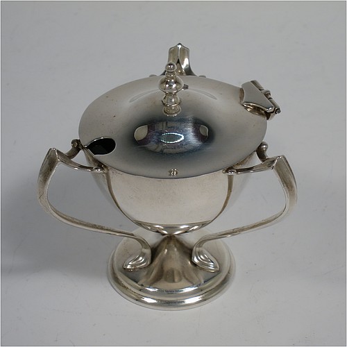 A very stylish Antique Edwardian Art Nouveau pair of mustard pots, having plain round bellied bodies, with hinged lids having cast urn finials, and three scroll side-handles attached to round pedestal feet, and with internal blue glass liners. Made by Edward Souter Barnsley of Birmingham in 1905. The dimensions of these fine hand-made antique silver mustard pots are height 8 cms (3 inches), diameter 5.5 cms (2.25 inches), and they weigh at total of approx. 164g (5.3 troy ounces).   