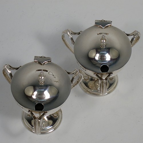 A very stylish Antique Edwardian Art Nouveau pair of mustard pots, having plain round bellied bodies, with hinged lids having cast urn finials, and three scroll side-handles attached to round pedestal feet, and with internal blue glass liners. Made by Edward Souter Barnsley of Birmingham in 1905. The dimensions of these fine hand-made antique silver mustard pots are height 8 cms (3 inches), diameter 5.5 cms (2.25 inches), and they weigh at total of approx. 164g (5.3 troy ounces).   