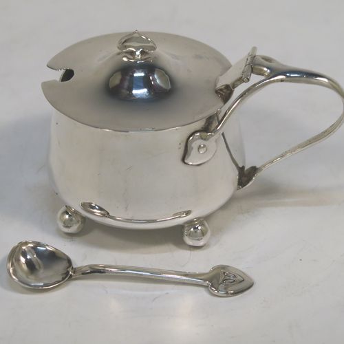 A very unusual Antique Edwardian Arts and Crafts style mustard pot and spoon, having a plain round bellied body, with a hinged lid, a tendril style side-handle, sitting on four ball feet, and with an internal blue glass liner, together with its original condiment spoon. This elegant antique silver mustard pot was made by James Fenton and Co., of Birmingham in 1906. The dimensions of these fine hand-made antique Art and Crafts silver mustard pot are height 5 cms (2 inches), diameter 6 cms (2.3 inches), and it weighs approx. 78g (2.5 troy ounces).   