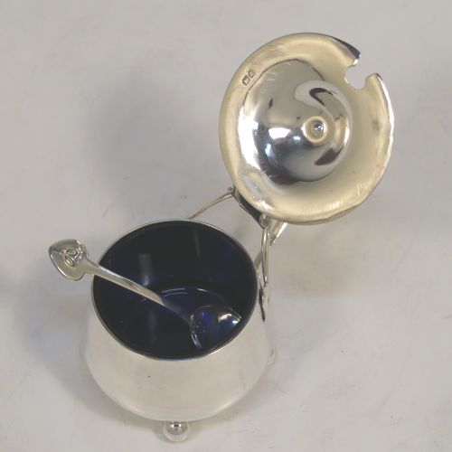 A very unusual Antique Edwardian Arts and Crafts style mustard pot and spoon, having a plain round bellied body, with a hinged lid, a tendril style side-handle, sitting on four ball feet, and with an internal blue glass liner, together with its original condiment spoon. This elegant antique silver mustard pot was made by James Fenton and Co., of Birmingham in 1906. The dimensions of these fine hand-made antique Art and Crafts silver mustard pot are height 5 cms (2 inches), diameter 6 cms (2.3 inches), and it weighs approx. 78g (2.5 troy ounces).   