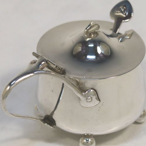 A very unusual Antique Edwardian Arts and Crafts style mustard pot and spoon, having a plain round bellied body, with a hinged lid, a tendril style side-handle, sitting on four ball feet, and with an internal blue glass liner, together with its original condiment spoon. This elegant antique silver mustard pot was made by James Fenton and Co., of Birmingham in 1906. The dimensions of these fine hand-made antique Art and Crafts silver mustard pot are height 5 cms (2 inches), diameter 6 cms (2.3 inches), and it weighs approx. 78g (2.5 troy ounces).   