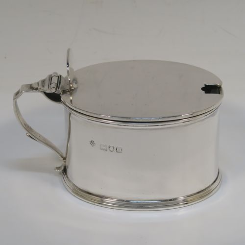 A very handsome Antique Edwardian Sterling Silver mustard pot, having a plain oval straight-sided body, with applied reeded borders, a flat hinged lid with an oval thumb-piece, a scroll side-handle, a blue-glass liner, and sitting on a flat base. This elegant antique silver mustard pot was made by Horace Woodward of London in 1909. The dimensions of this fine hand-made antique silver mustard pot are length 10 cms (4 inches), height 6.5 cms (2.75 inches), and it weighs approx. 132g (4.3 troy ounces).   