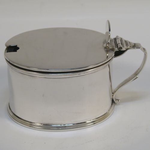 A very handsome Antique Edwardian Sterling Silver mustard pot, having a plain oval straight-sided body, with applied reeded borders, a flat hinged lid with an oval thumb-piece, a scroll side-handle, a blue-glass liner, and sitting on a flat base. This elegant antique silver mustard pot was made by Horace Woodward of London in 1909. The dimensions of this fine hand-made antique silver mustard pot are length 10 cms (4 inches), height 6.5 cms (2.75 inches), and it weighs approx. 132g (4.3 troy ounces).   