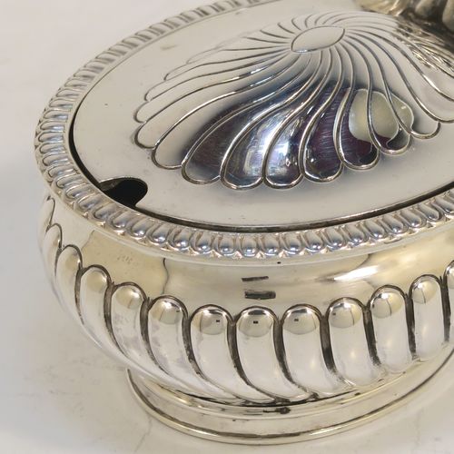 A beautiful Antique Victorian Sterling Silver mustard pot, having an oval bellied body with hand-chased fluted decoration, a gadroon-edged border, a hinged lid with cast scroll thumb-piece, a blue glass liner and scroll handle, all sitting on a collet foot. This very pretty antique silver mustard pot was made by Edward Hutton of London in 1891. The dimensions of this fine hand-made silver mustard pot are height 5.5 cms (2.25 inches), length 10.5 cms (4.25 inches), width 6.5 cms (2.5 inches), and it weighs approx. 142g (4.6 troy ounces).   