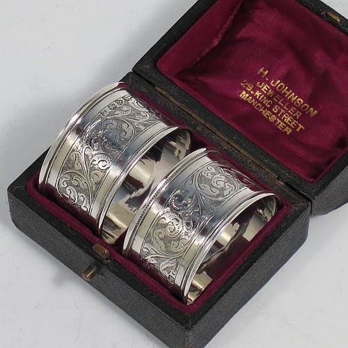 A very pretty Antique Victorian Sterling Silver pair of napkin rings, having round straight-sided bodies with applied borders, each one hand-engraved with a band of floral and scroll-work decoration, with shield-shaped vacant cartouches, and all in their original maroon satin and velvet-lined presentation box. Made by the Deakin Brothers of Chester in 1896. The dimensions of these fine hand-made antique silver napkin rings are diameter 4.5 cms (1.75 inches), height 2.5 cms (1 inch), and they weigh a total of approx. 36g (1.2 troy ounces).    