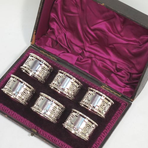 A pretty Antique Sterling Silver set of six napkin rings, having round straight-sided bodies, with hand-pierced geometrical style decoration, a central oval vacant cartouche, and with applied faceted borders, all in their original maroon satin and velvet-lined presentation box. Made by Ferganbaum and Son of Birmingham in 1921. The dimensions of these fine hand-made silver napkin rings are diameter 4.5 cms (1.75 inches), height 2.5 cms (1 inch), and they weigh a total of approx. 140g (4.5 troy ounces). 