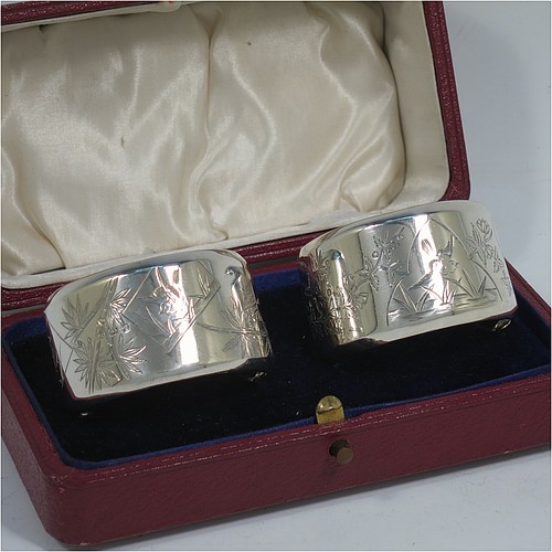 A very pretty Antique Victorian Aesthetic style Sterling Silver pair of napkin rings, having round straight-sided bodies with turned-over borders, and each one hand-engraved differently with Aesthetic decoration of birds, butterflies and bamboo shoots, all in their original cream satin and dark blue velvet-lined presentation box. Made by George Unite of Birmingham in 1881. The dimensions of these fine hand-made antique silver napkin rings are diameter 5 cms (2 inches), height 3 cms (1.25 inches), and they weigh a total of approx. 48g (1.5 troy ounces).    