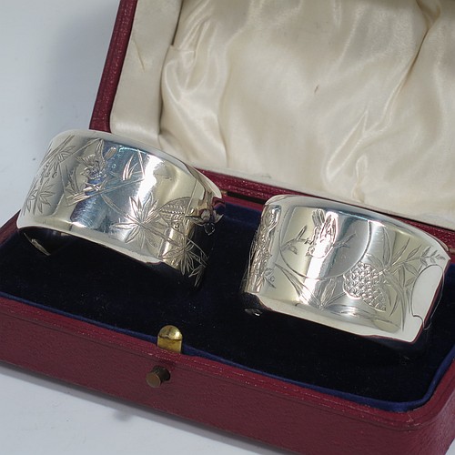 A very pretty Antique Victorian Aesthetic style Sterling Silver pair of napkin rings, having round straight-sided bodies with turned-over borders, and each one hand-engraved differently with Aesthetic decoration of birds, butterflies and bamboo shoots, all in their original cream satin and dark blue velvet-lined presentation box. Made by George Unite of Birmingham in 1881. The dimensions of these fine hand-made antique silver napkin rings are diameter 5 cms (2 inches), height 3 cms (1.25 inches), and they weigh a total of approx. 48g (1.5 troy ounces).    