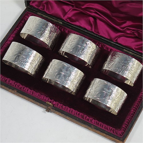 A very pretty Antique Victorian Sterling Silver set of six napkin rings, having oval-shaped bodies with straight sides and hand-engraved ferns and gingko leaves surrounding a cartouche on one side, all in their original maroon satin and velvet-lined presentation box. Made by Edward Hutton of London in 1891. The dimensions of these fine hand-made antique silver napkin rings are length 5 cms (2 inches), height 3 cms (1.25 inch), and they weigh a total of approx. 166g (5 troy ounces). Please note that these items are crested and numbered 1 to 6.   