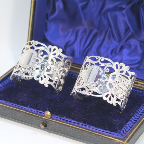 A very pretty Antique Edwardian Art Nouveau style Sterling Silver pair of napkin rings, having round straight-sided bodies with hand-pierced and engraved floral and scroll decoration, all in their original dark blue satin and velvet-lined presentation box. These beautiful antique silver napkin rings were made by George Rhoden of Sheffield in 1909. The dimensions of these fine hand-made antique silver napkin rings are diameter 4.5 cms (1.75 inches), height 4 cms (1.5 inches), and they weigh a total of approx. 63g (2 troy ounces).   