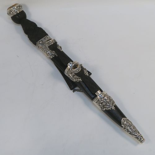 A beautiful and large sterling silver, black leather, and carved wooden Scottish Dirk holder, having hand-chased silver mounts with thistle decoration, carved hard-wood handles, a leather scabbard, smoky Citreen handle tops, removable main knife, eating knife and fork with stainless steel blades and security chains, and a black leather belt loop. This handsome silver, wood, and leather Dirk holder was made by Anthony Holland of Edinburgh in 1978. The dimensions of this fine hand-made Scottish sterling silver Dirk holder are lenght 49 cms (19.25 inches) and width 5 cms (2 inches).