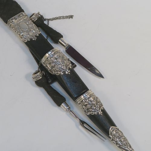 A beautiful and large sterling silver, black leather, and carved wooden Scottish Dirk holder, having hand-chased silver mounts with thistle decoration, carved hard-wood handles, a leather scabbard, smoky Citreen handle tops, removable main knife, eating knife and fork with stainless steel blades and security chains, and a black leather belt loop. This handsome silver, wood, and leather Dirk holder was made by Anthony Holland of Edinburgh in 1978. The dimensions of this fine hand-made Scottish sterling silver Dirk holder are lenght 49 cms (19.25 inches) and width 5 cms (2 inches).