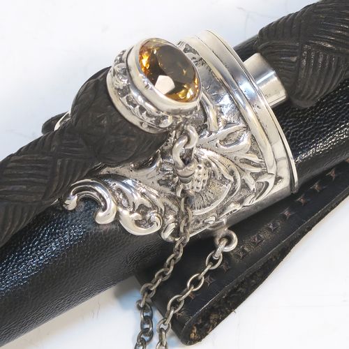 A beautiful and large sterling silver, black leather, and carved wooden Scottish Dirk holder, having hand-chased silver mounts with thistle decoration, carved hard-wood handles, a leather scabbard, smoky Citreen handle tops, removable main knife, eating knife and fork with stainless steel blades and security chains, and a black leather belt loop. This handsome silver, wood, and leather Dirk holder was made by Anthony Holland of Edinburgh in 1978. The dimensions of this fine hand-made Scottish sterling silver Dirk holder are lenght 49 cms (19.25 inches) and width 5 cms (2 inches).