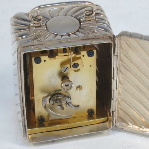 A very pretty Antique Victorian Sterling Silver carriage clock, having a rectangular upright body with hand-chased swirl-fluted decoration, with a hinged back door opening to the original clock movement mechanism and winder, a hinged and scrolled top carrying handle, and all sitting on four cushion feet. Made by Louis Augustus Leins of London in 1897. The dimensions of this fine hand-made antique silver carriage clock are height 7.5 cms (3 inches), width 5.5 cms (2.25 inches), and depth 4.5 cms (1.75 inches). Please note that this clock has been serviced and works properly.   